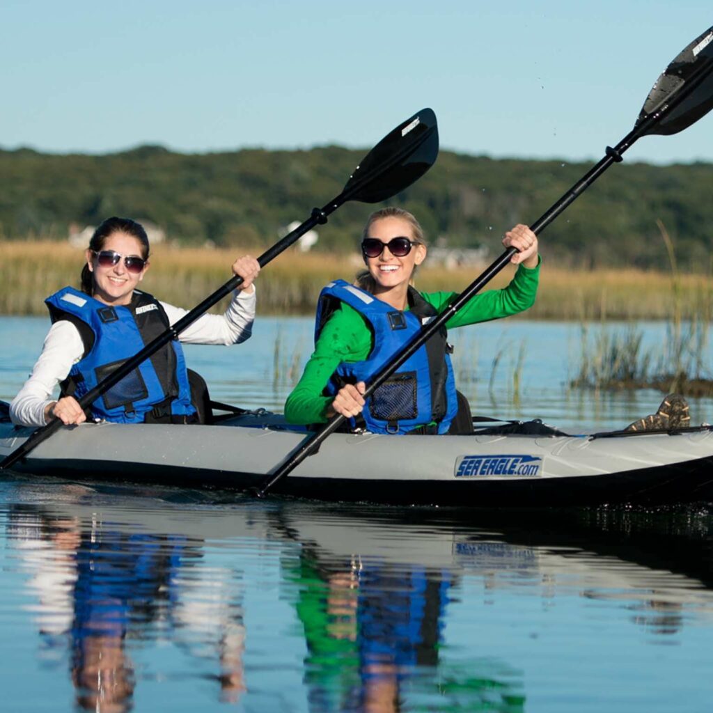 Two smiling women paddle an inflatable kayak